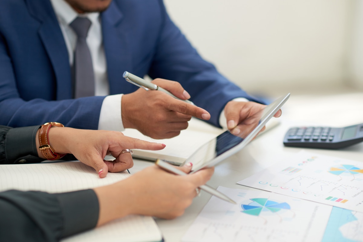 Duas pessoas estão sentadas lado a lado em uma mesa, analisando documentos.