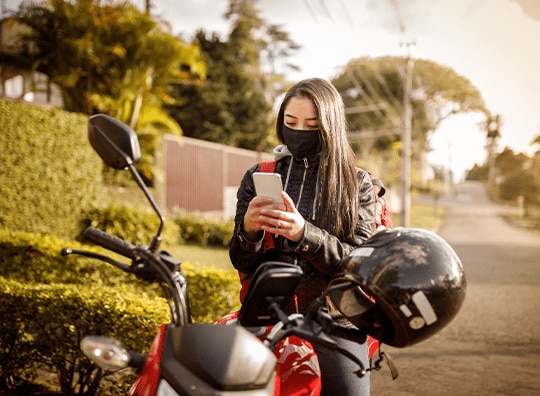 mulher sentada na moto parada e mexendo no celular