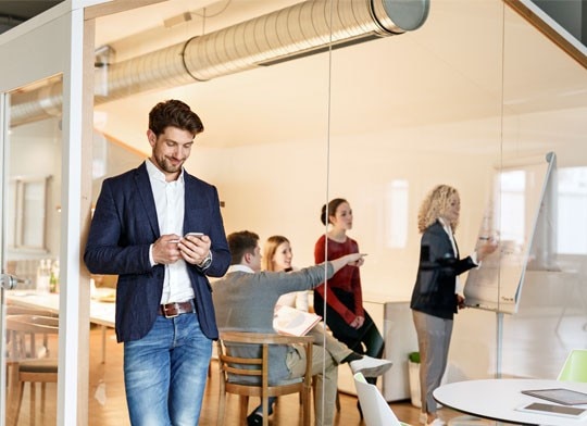 Homem utilizando seu celular enquanto um grupo de pessoas trabalham.