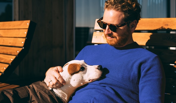 Cliente Itaú de óculos escuros, com seu cachorro no colo, enquanto está sentado em uma espreguiçadeira