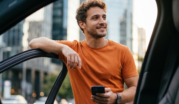 Homem ao lado de veículo utiliza celular na cidade.