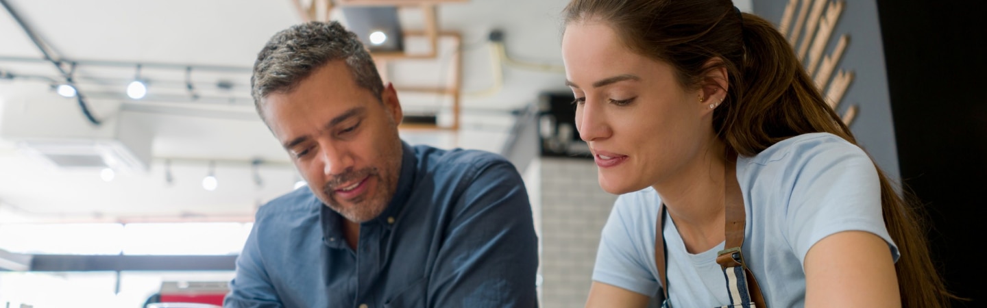 homem e mulher sentados em uma mesa conversando e analisando alguns papeis