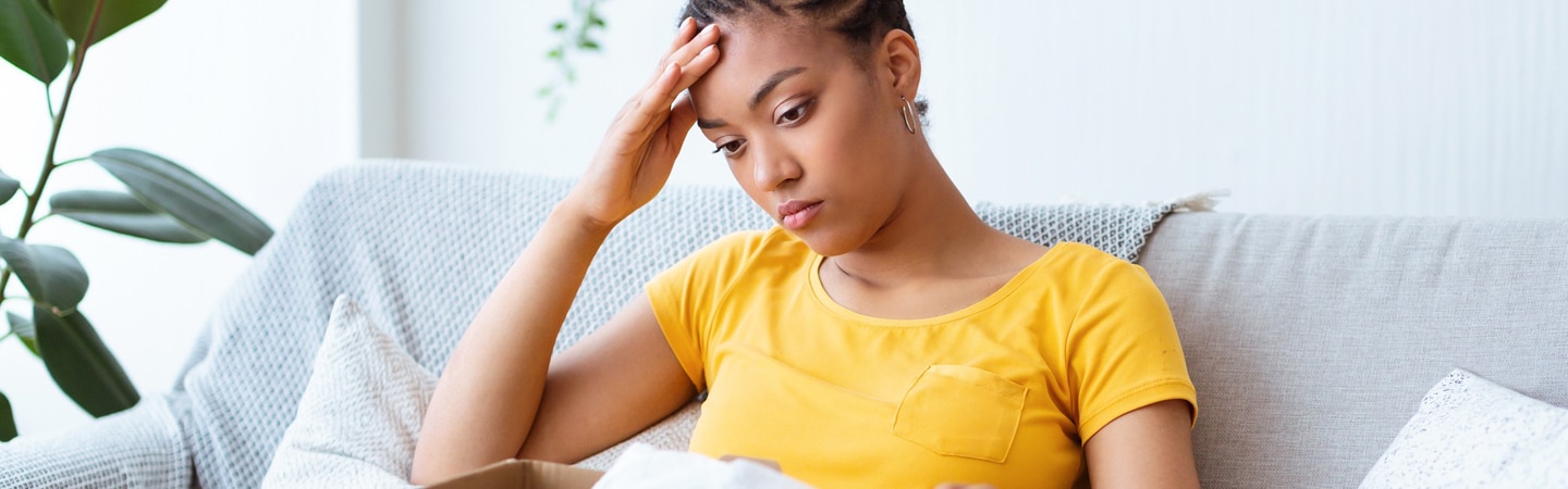 mulher sentada em um sofá segurando uma caixa nos braços pensando em como solicitar o cancelamento de uma compra