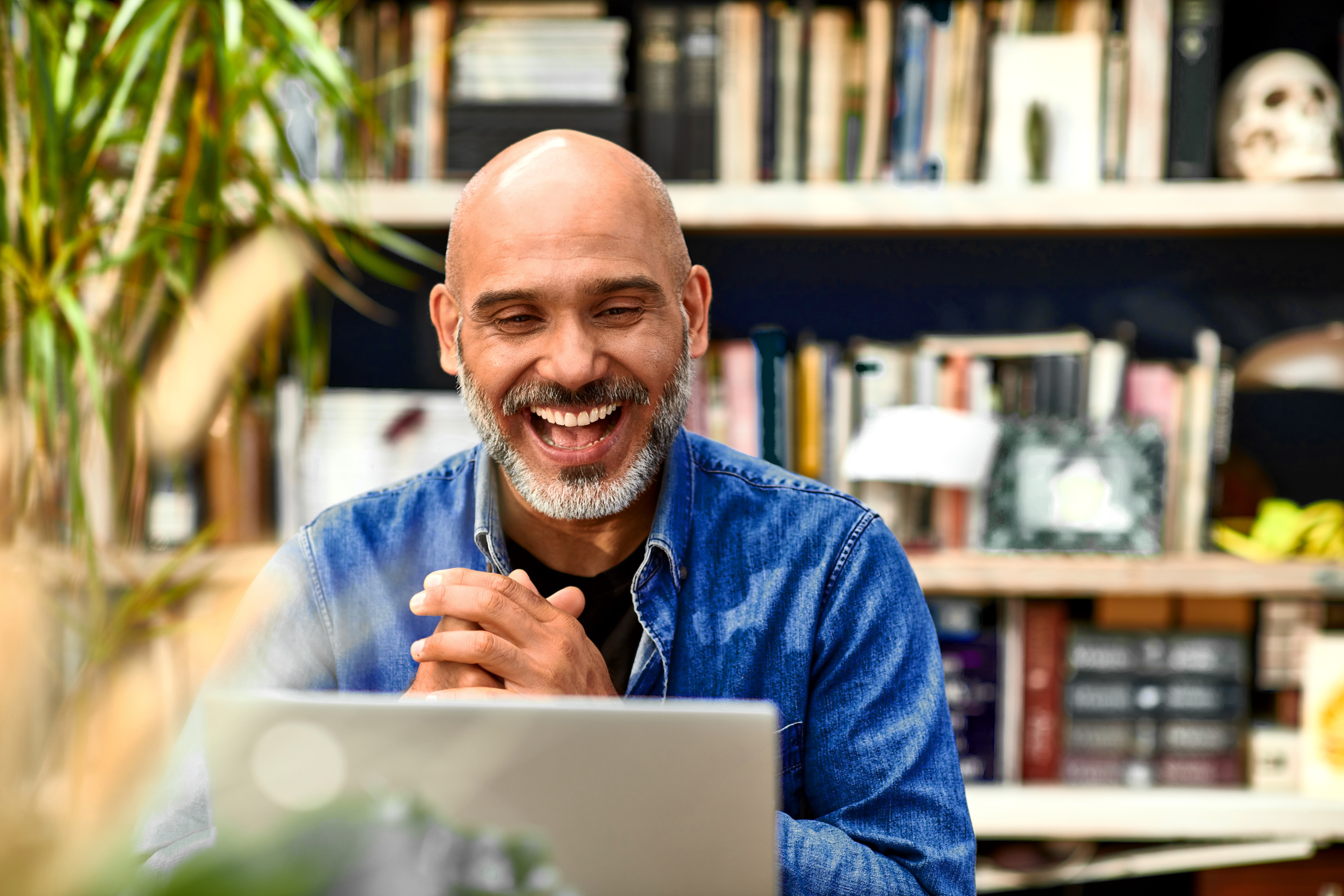 Um homem negro, grisalho, olha para seu laptop enquanto abre um sorriso.