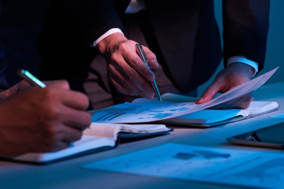 Pessoas analisando documentos financeiros e relatórios em uma mesa de trabalho, com foco em planejamento e organização das finanças empresariais.