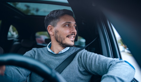 Imagem de um homem dirigindo olhando pela janela lateral do automóvel.