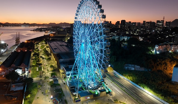 Roda-gigante iluminada ao entardecer com cidade e mar.