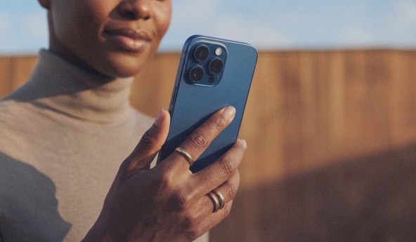 Pessoa segura smartphone azul em ambiente externo desfocado.