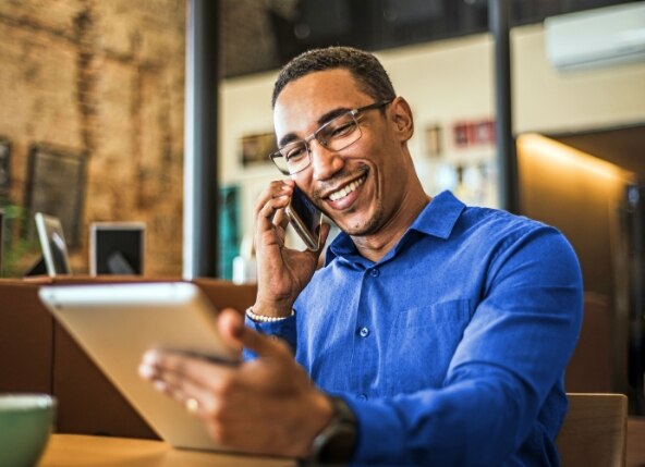 homem sorrindo, usando tablet e celular