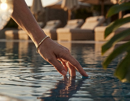 Mão toca a água de uma piscina ao ar livre.