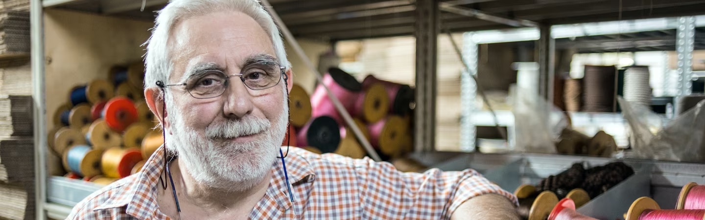 Senhor encostado em uma estante com vários carreteis de linha