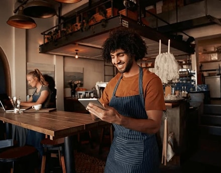 Pessoa com avental usando tablet atrás de balcão em cafeteria.
