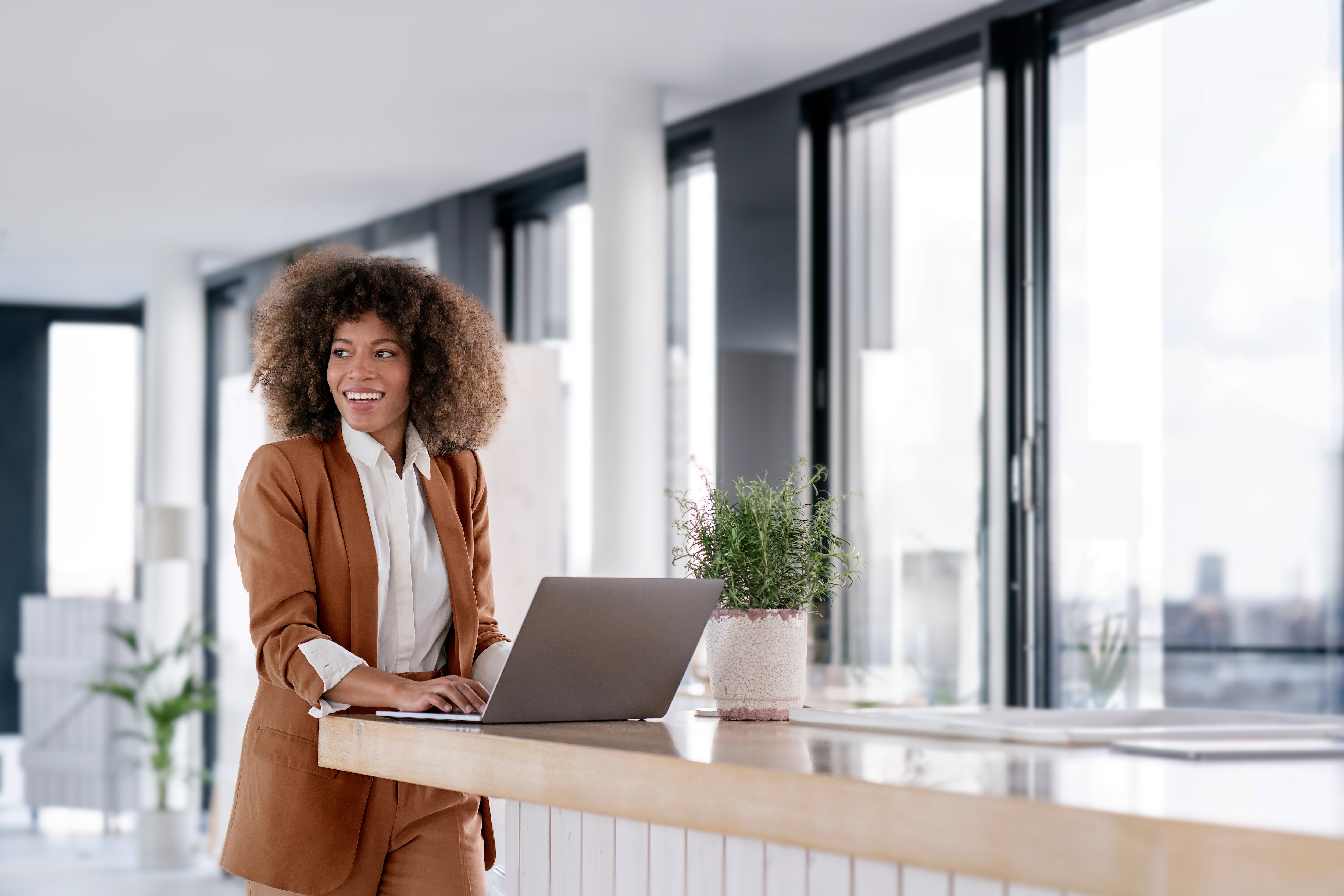 Mulher cliente Itaú Private Bank em pé em frente a uma mesa, com um notebook aberto e sorrindo.
