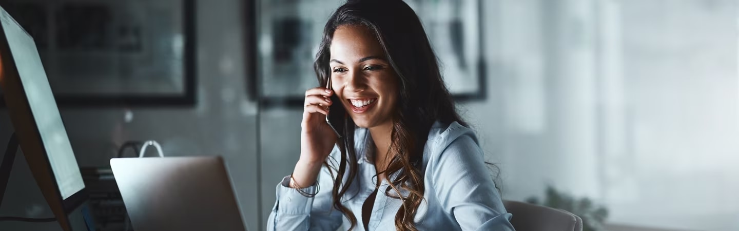 Mulher falando ao telefone em frente ao computador e um notebook