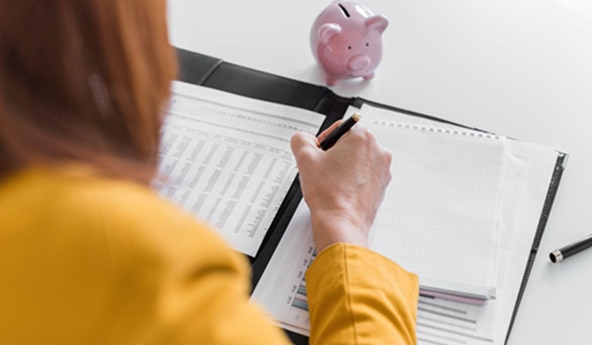 Uma mulher fazendo anotações das economias, representando a educação financeira.
