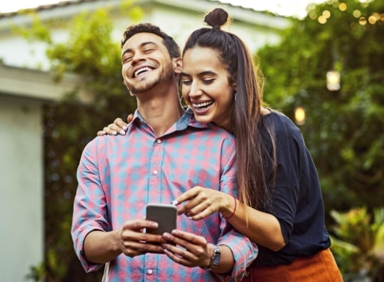Casal clientes Itaú Uniclass juntos sorrindo olhando para o celular